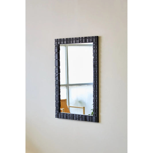 Vertical mirror with black frame on grey wall.
